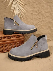 Détail de bottines grises aspect daim avec fermeture éclair latérale dorée fonctionnelle