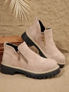 Détail de bottines en daim beige avec fermeture éclair dorée et semelle crantée noire.