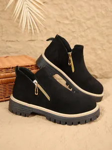Gros plan de bottines en daim noir avec fermeture éclair dorée et semelle plateforme épaisse.