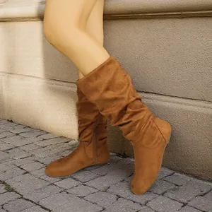 Stylish brown suede slouchy boots with round toe and side zipper shown on a street.