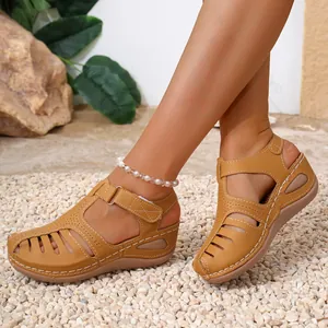 Side detail of women's tan closed-toe wedge sandals with white stitching and hollow design