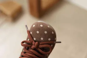 Close-up detail of children's brown suede boots with white polka dots and bow tie laces