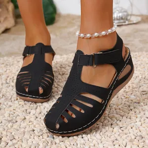 Close-up of black wedge sandals featuring closed toe and white stitching on gravel ground
