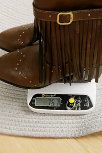 Detail shot of brown fringe cowboy boots showing product weight on a digital scale