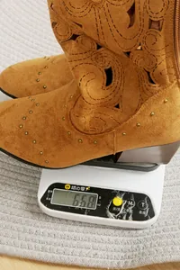 Detail view showing weight of brown suede western cowboy boot with rivets on a scale