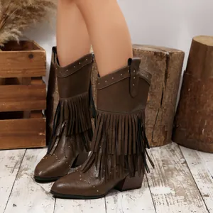 Detailed view of brown fringe cowboy boots with rivets in a rustic wooden setting