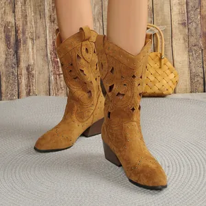 Detail view of tan suede cowboy boots featuring intricate cutouts and gold metal studs