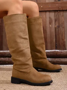Detailed view of women's brown suede high-top boots styled with a rustic wooden backdrop