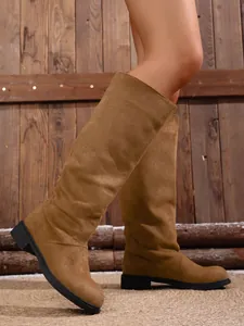 Detailed side view of brown suede tall boots with low heel on rustic wooden background
