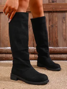Close-up of women's black suede knee-high fashion boots with low heel.