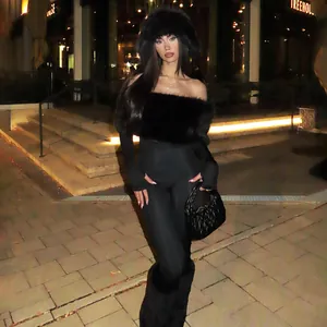 Model wearing a sexy black off-shoulder jumpsuit with faux fur trim in a night street setting.