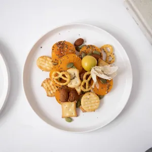Minimalist white ceramic dinner plate styled with a variety of healthy snacks and nuts