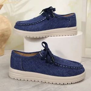 Detailweergave van blauwe denim loafers met witte stiksels en dikke beige zolen.