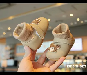 Close-up of warm beige baby walking shoes with cute plush bear patch and knit cuffs.