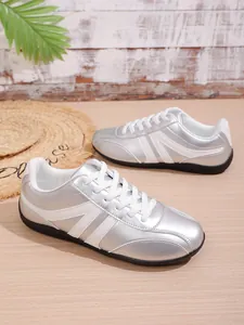 Silver metallic sneakers with white side stripes and lace-up closure on a wooden surface.
