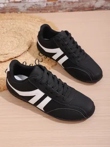 Detailed view of stylish black casual sneakers with white stripes on wooden floor