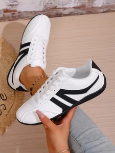 Close-up of women's white casual sneakers with black stripes on wooden background