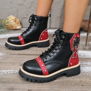 Détail rapproché de bottines noires à plateforme avec bordure rouge, clous et chaîne tête de mort.