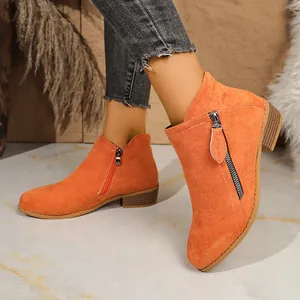 Detailopname van feloranje suède enkellaarsjes met een stijlvol ritsdetail aan de zijkant