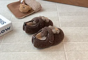Dettaglio scarpe in peluche marroni per bambine con fiocco carino e toppa fatta a mano.