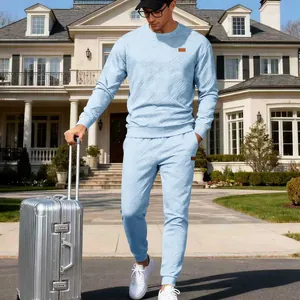 Lifestyle detail of men's blue jacquard tracksuit set with model holding a silver suitcase