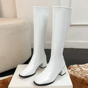 Detailed macro view of white patent leather knee-high boots with a square toe design