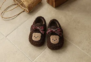 Nahaufnahme gemütlicher brauner flauschiger Kleinkinderschuhe mit roten Schleifen