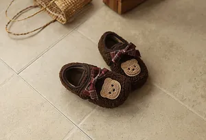 Detailansicht gemütlicher brauner Pelz-Babyschuhe mit Karo-Schleife und süßem Bären-Patch