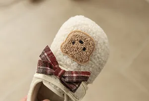 Detail eines flauschigen Kinder-Fleece-Schuhs mit roter Karoschleife und Bären-Patch