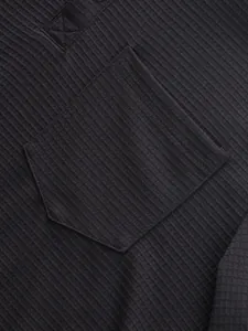 Close-up detail of the black ribbed fabric texture and chest pocket on a men's Henley shirt