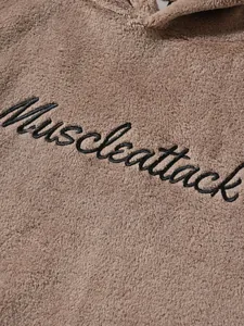 Close-up of black cursive Muscleattack embroidery on fuzzy brown hoodie texture