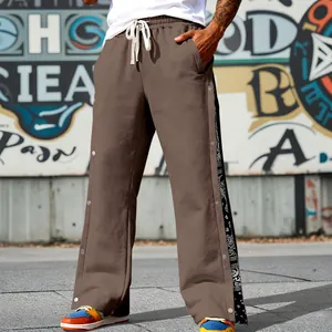 Detail view of men's brown wide-leg snap button sweatpants with paisley side panel