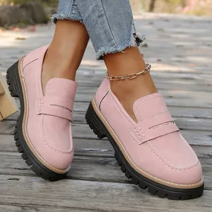 Close-up of pink nubuck loafers with thick black platform soles on a wooden path