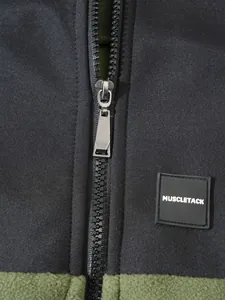 Detailansicht eines Metallreißverschlusses und MUSCLETACK-Aufnähers auf Fleecejacke.