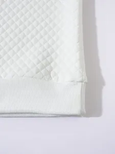 Détail macro d'un sweat-shirt blanc matelassé avec ourlet côtelé et motif en losange.