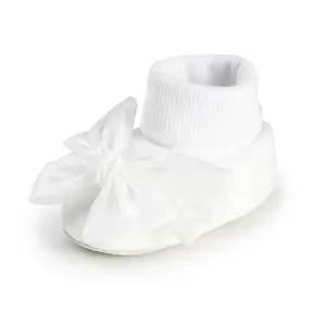 Detail view of a white baby sock featuring a large satin bow and ribbed cuff textures.