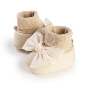 Close-up detail of cream baby booties featuring a large elegant satin bow for infants
