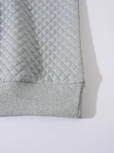 Gros plan sur la texture gaufrée grise matelassée et l'ourlet côtelé du sweat-shirt
