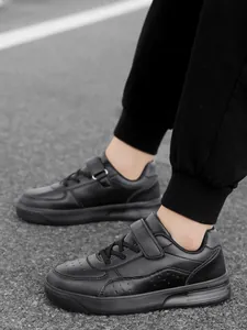 Detailed view of children's black low-top sneakers with velcro strap and laces