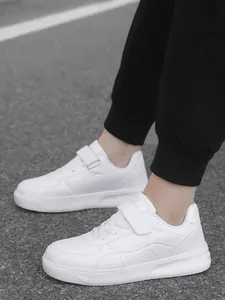 On-feet view of children's white low-top sneakers with velcro straps on asphalt