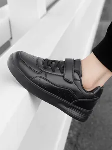 Detailed side view of black children's low-top athletic sneakers featuring laces and strap