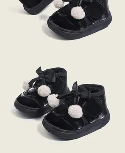 Detailed view of black children's winter warm shoes with white pompoms and decorative bows