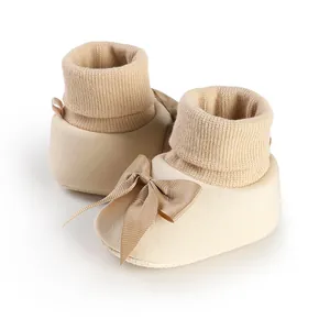 Vue détaillée de chaussons pour bébé beige avec bord-côte souple et un élégant nœud en soie.