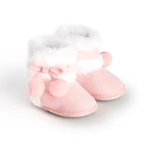 Close-up view of pink soft-sole baby booties featuring white faux fur trim and cute pom-poms