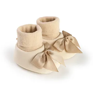 Chaussons-chaussettes bébé en tricot beige avec un grand nœud en satin décoratif.
