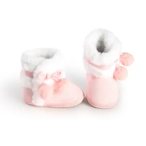 Detail shot of pink faux fur baby boots with soft soles and decorative pom-poms.