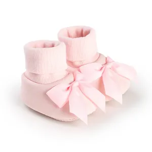 Gros plan de chaussons pour bébé rose tendre avec un grand nœud en ruban satiné.