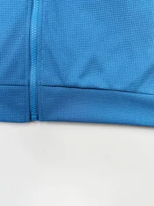 Gros plan d'une veste en tricot bleu gaufré avec fermeture éclair et ourlet assortis.