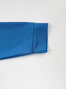 Détail macro du poignet en maille gaufrée bleue sur une veste ajustée pour homme