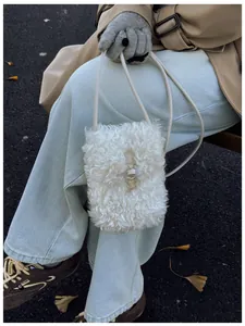 Detail of a white fuzzy teddy fleece crossbody bag worn with a winter trench coat.
